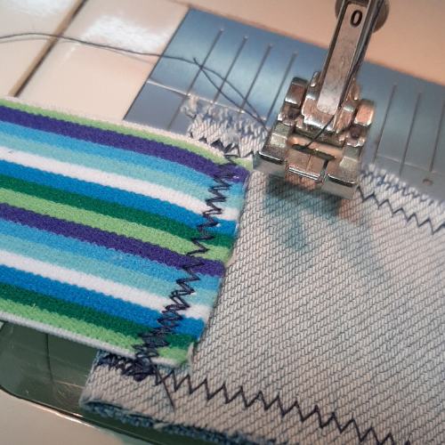 Foto zum dritten Schritt für eine selbstgenähte Bechermanschette: Jeansstoff und Hosengummi unter der Nähmaschine