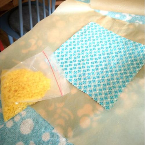 Foto zum ersten Schritt für ein selbstgemachtes Wachstuch: Baumwolltuch auf Backpapier, daneben eine Tüte mit Wachs