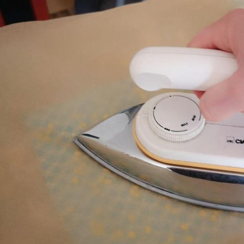 Foto zum dritten Schritt für ein selbstgemachtes Wachstuch: Bügeleisen auf Backpapier, darunter ein mit Wachs bestreutes Tuch