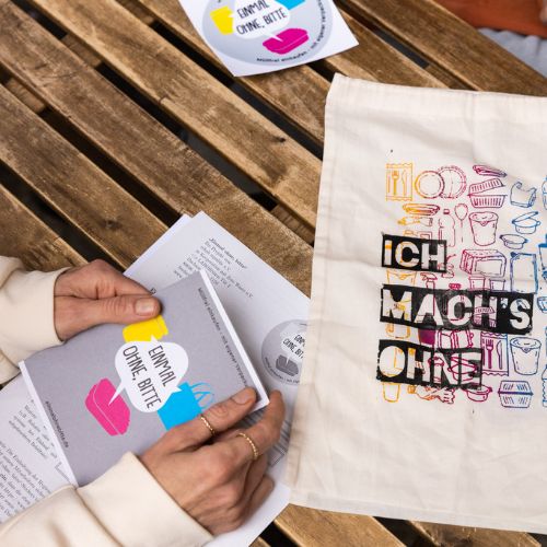 Person bei der Durchsicht von Ansichtsmaterial von „Einmal ohne, bitte“ wie Dokument, Flyer, Sticker und bedrucktem Stoffbeutel