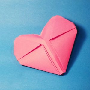 Foto eines aus Papier gefalteten rosa Herzens auf blauem Hintergrund