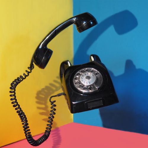 Altes Wählscheibentelefon in Schwarz vor buntem Hintergrund als Symbolbild für die Kontaktaufnahme