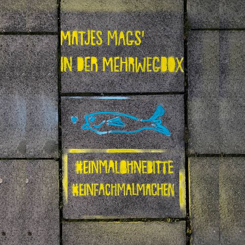 Auf den Gehweg gesprayter Text: „Matjes mag’s in der Mehrwegbox“, darunter ein Fisch und die Hashtags „Einmal ohne, bitte“ und „Einfach mal machen“