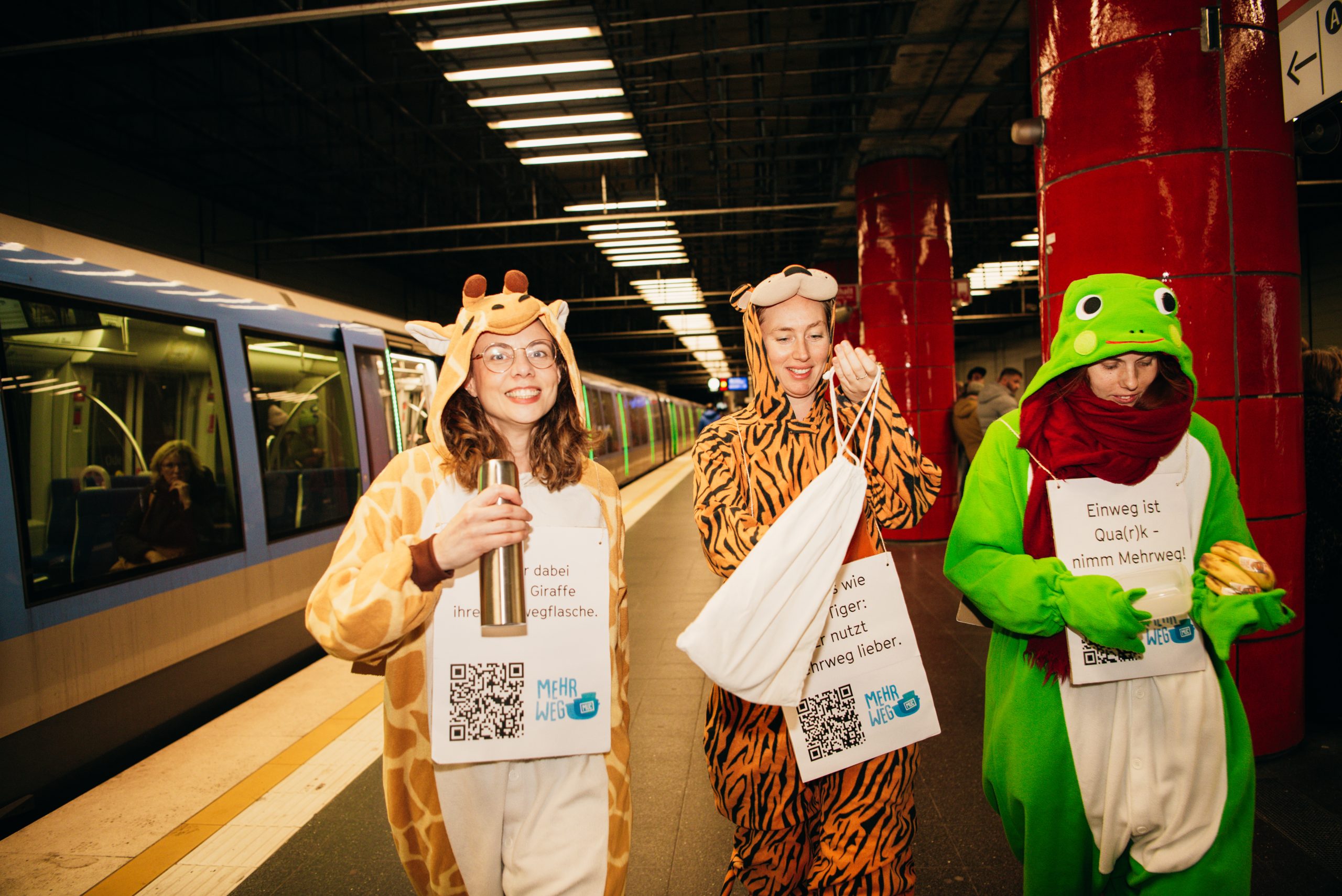 Foto von drei Personen in Tierkostümen und mit eigenen Behältnissen als „Mehrweg-Gang“ bei einer Sensibilisierungsaktion in der Münchner U-Bahn