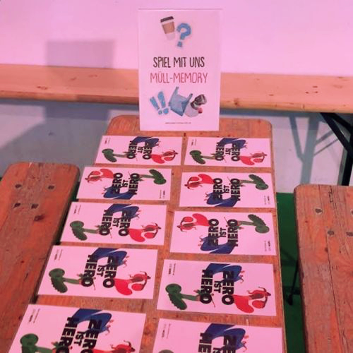 Bild, das einen Aufsteller mit dem Text „Spiel mit uns Müll-Memory“ und auf einem Tisch ausgebreitete Memory-Karten zeigt