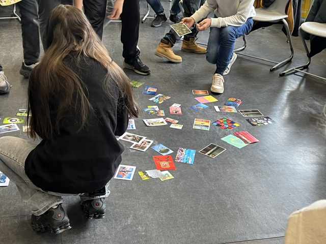 Foto von bunten Postkarten, die Kinder im Rahmen einer Kennenlernrunde vom Boden aufheben